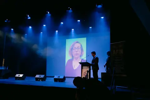 The SunPAC stage under blue lights during the AFIN Awards Night, a filmmaker accepting on the big screen.